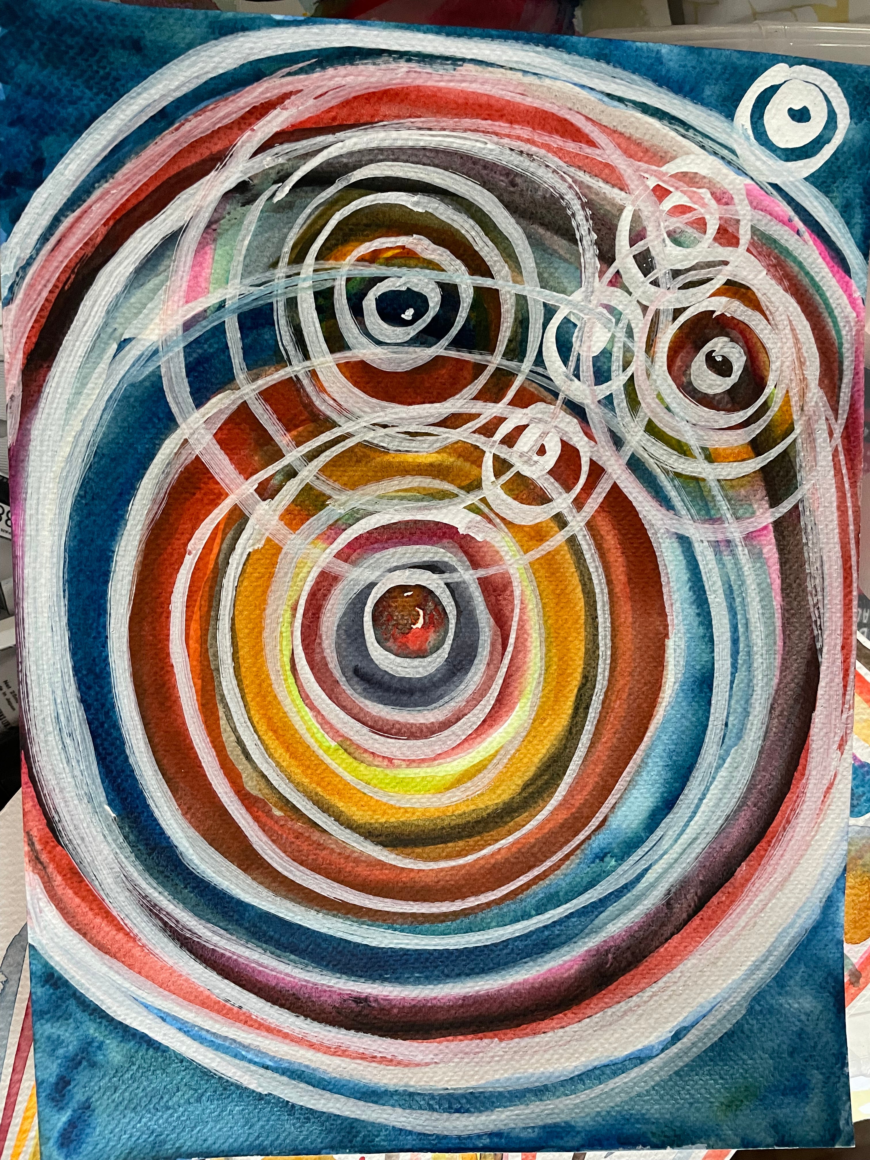 Abstract circular painting with concentric rings in blue, red, orange, yellow, brown, and white, plus several white spiral marks on a textured canvas.